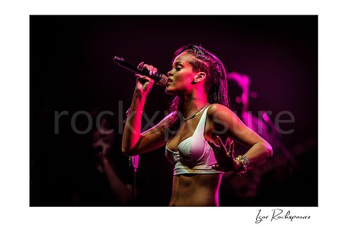Horizontal color image of Rihanna singing into a microphone in side profile under vivid magenta stage lighting