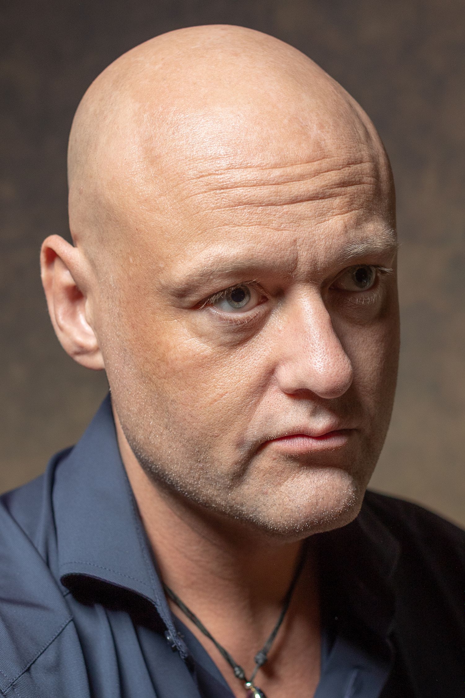 Close-up portrait of a bald man in a navy shirt with soft studio lighting, photographed in Stockholm by Mats Karlsson.