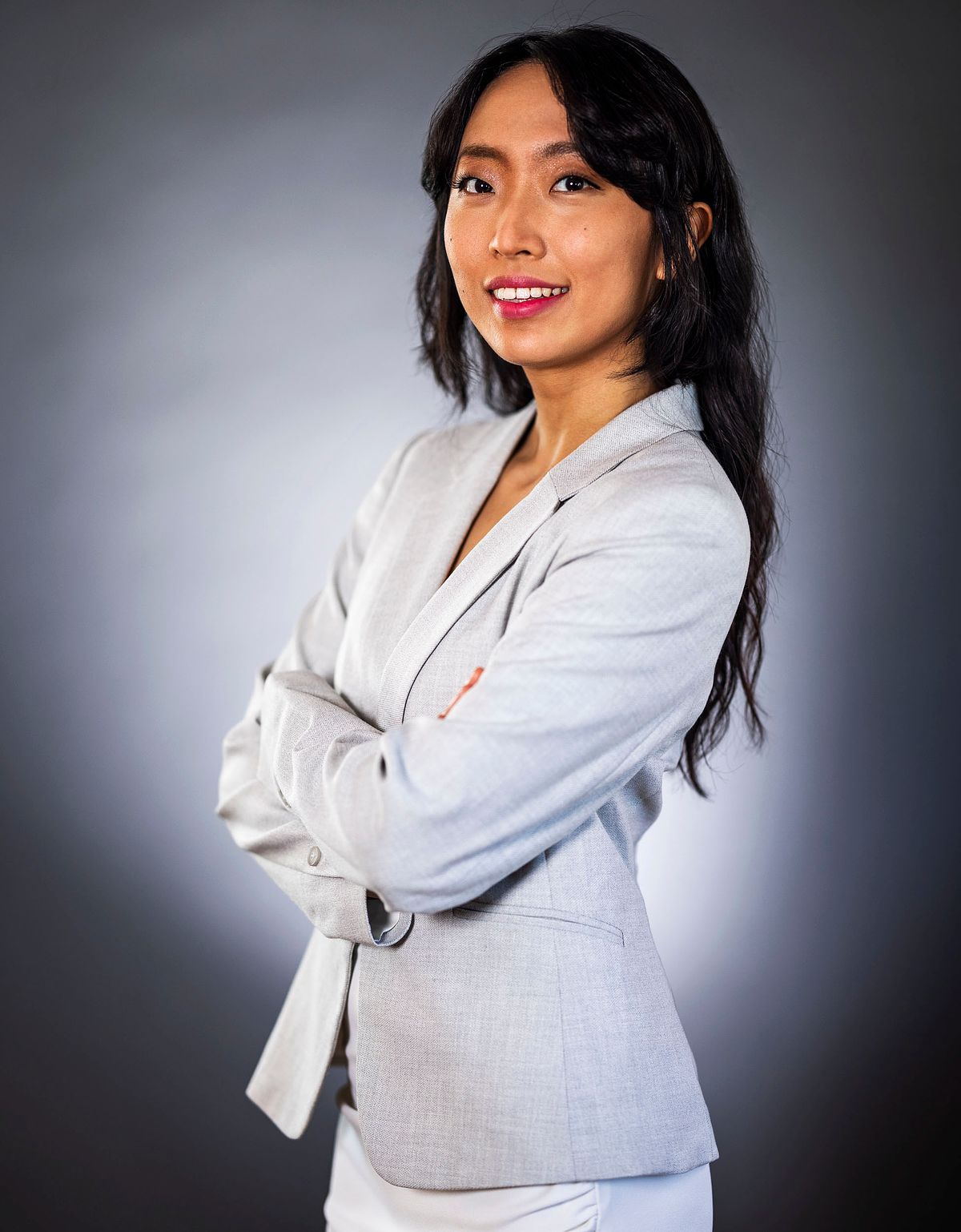 Corporate portrait of a female Asian business woman wearing a grey suit against a dark background.