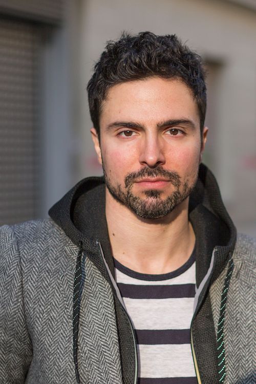 Toni Gojanovic in a gray jacket and striped hoodie standing on the street.