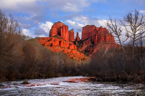 A dramatic fine art photograph of Castle Rock in Sedona, Arizona, captured during the "golden hour" sunset where the red sandstone glows with intense natural light against a deep blue sky