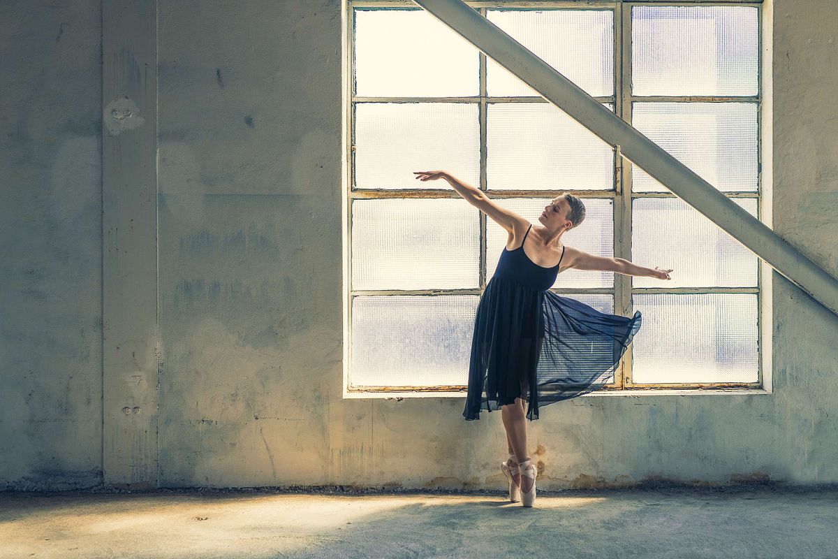 femme en robe de ballerine noire dans b&acirc;timent industriel, sur pointes, &eacute;clair&eacute;e par la lumi&egrave;re naturelle, photographie artistique