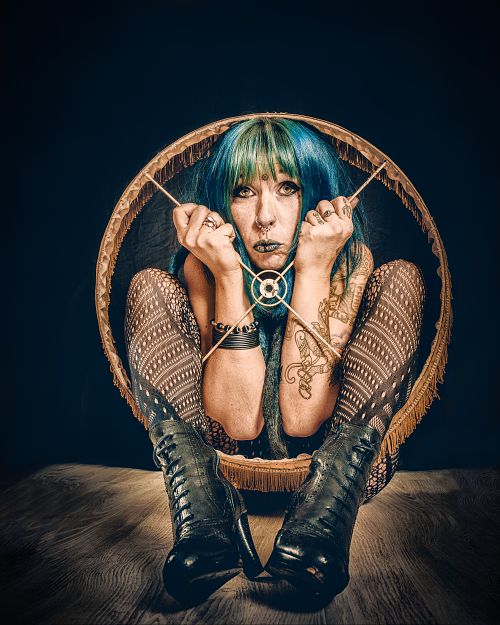 Portrait artistique d&rsquo;une femme aux cheveux color&eacute;s accroupie dans un abat-jour, symbolisant l&rsquo;enfermement psychologique, la prison mentale et la lutte pour se lib&eacute;rer &mdash; &oelig;uvre de Pascal Yennis, Namur, Belgique.