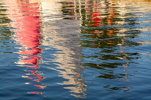 Colorful sailboats are reflected in water at sunset