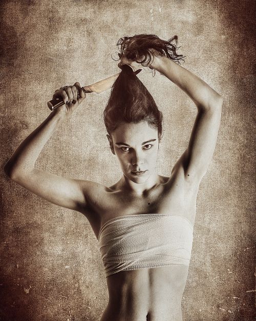 Portrait d'une femme compressant sa poitrine et se coupant les cheveux avec un couteau, exprimant la lutte identitaire et la dualité de genre — photographie fine art par Pascal Yennis, Namur, Belgique.