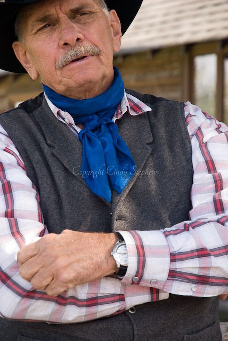 Tom Angle, a cowboy, rancher, and singer, poses thoughtfully in a cowboy hat, blue bandana, and plaid shirt, reflecting deep contemplation in Wyoming.