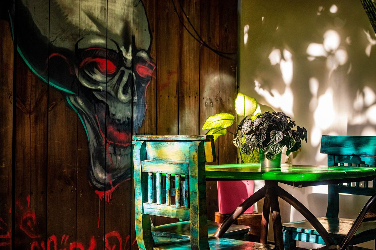 Artistic hotel corner with mural skull art, green chairs, and a potted plant in soft sunlight.