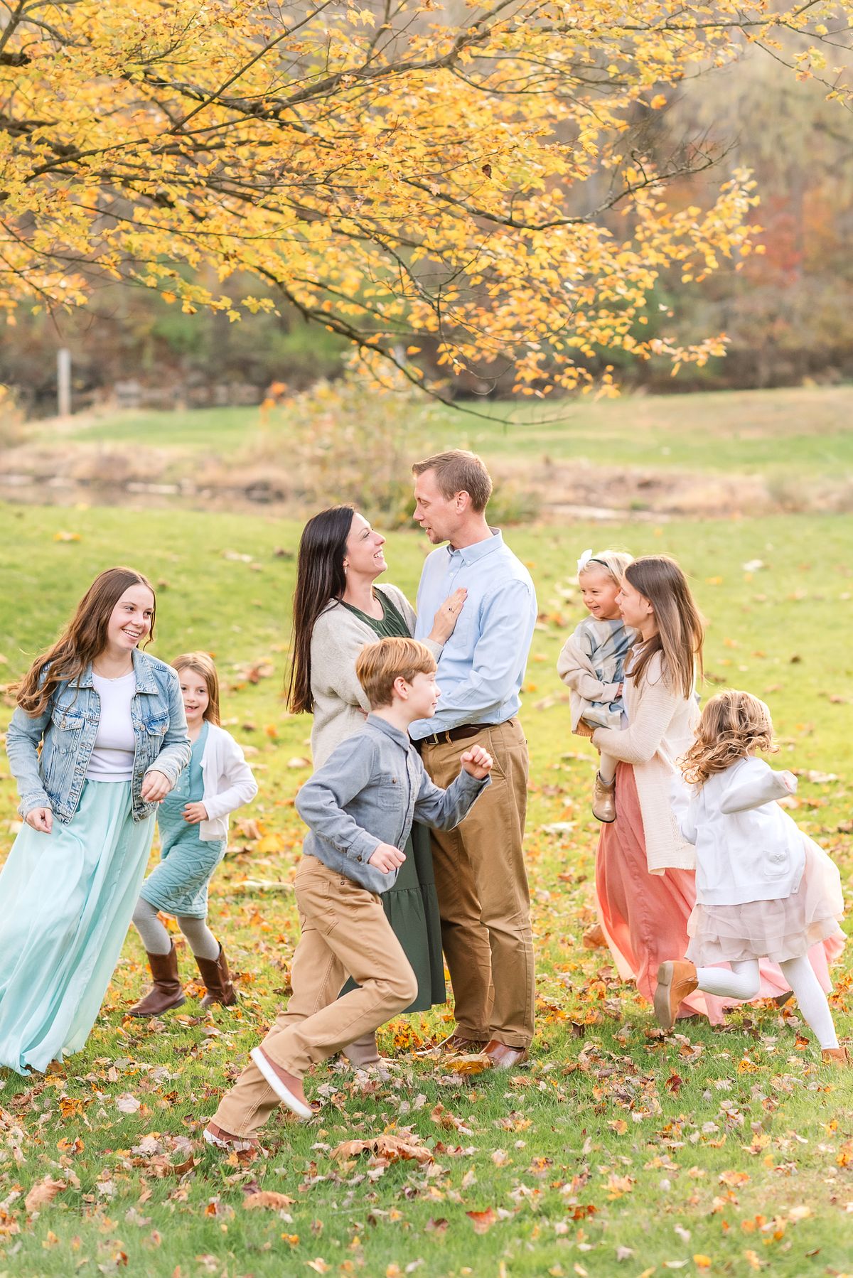 Husband and wife smiling at each other with their children running around with Cranberry Township, PA newborn photographer