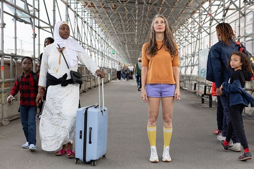 Kvinna står mitt i gångtunnel medan människor med bagage passerar