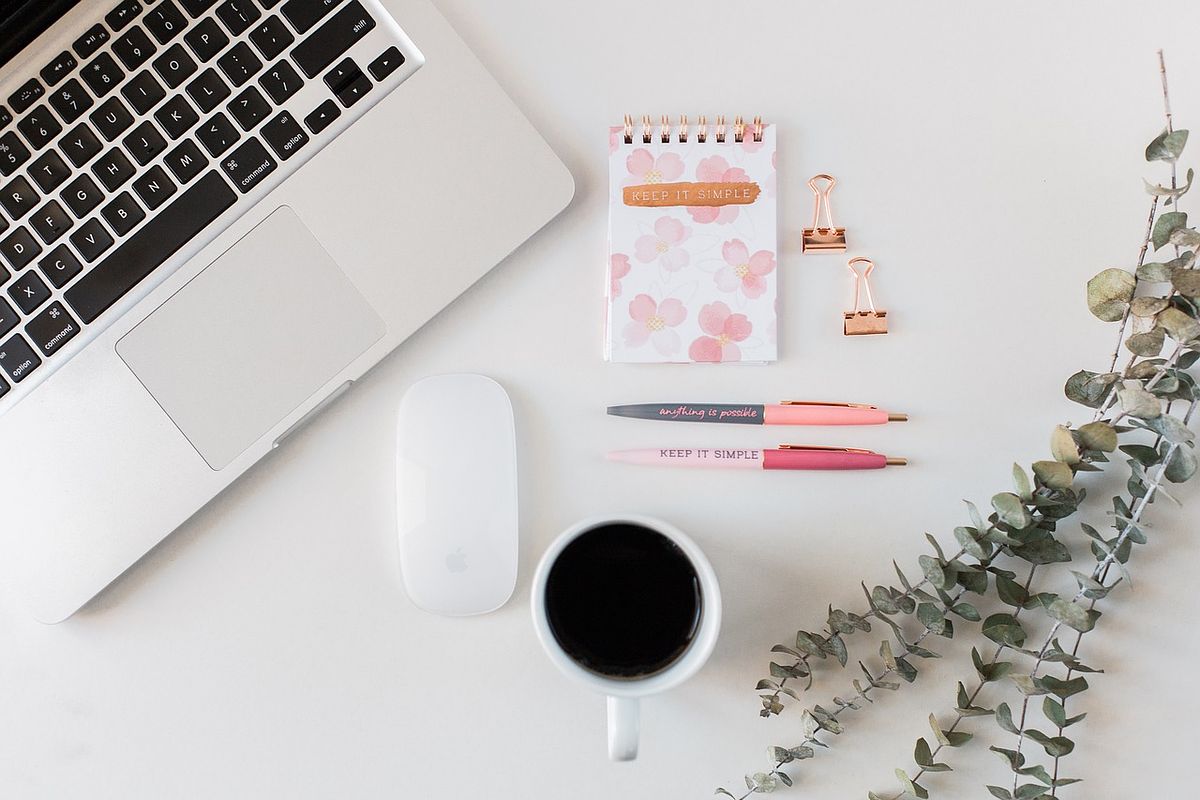 flat lay of a laptop, coffee mug, stationary and a dried eucalyptus on a white desk