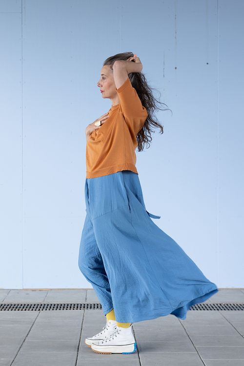 Profilporträtt för personal branding – person i orange topp och blått plagg mot ljusblå vägg.