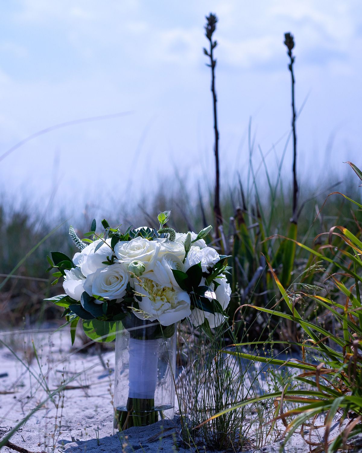 small wedding bouquet placed on the sand on the beach at assateague island, with stalks of yucca behind the flowers