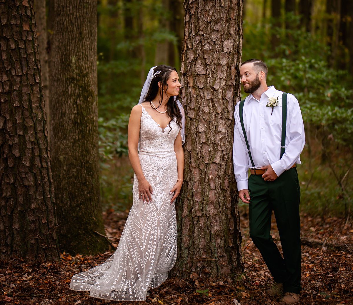 Groom and bride looking at each other standing next to a tree in the forest after the wedding ceremony