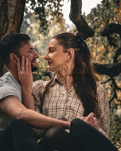 Alex and Shelby sitting under a tree during their engagement shoot, with the bride-to-be lovingly placing her hand on the groom-to-be’s face, captured by Weddings by Jermaine