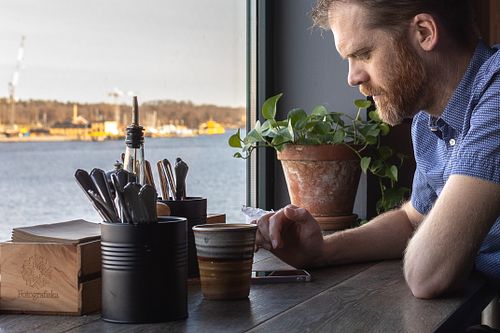 Lifestyle portrait of a man sitting at a café table by a window overlooking water, photographed in Stockholm by Mats Karlsson.