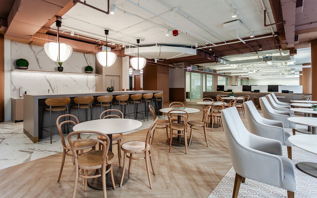Modern office cafe at 1 South Wacker featuring a marble-clad bar, high-top wooden bar stools, white circular dining tables, and designer dome pendant lighting with an open-office background