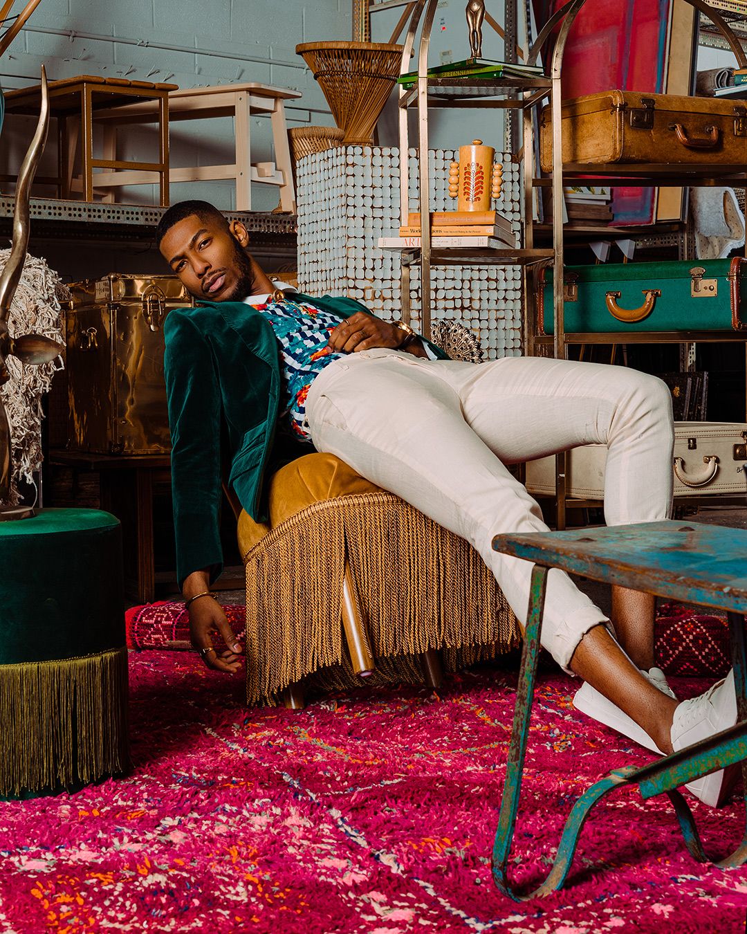 Brightly colored portrait of a male model in a green velvet jacket inspired by a Gucci campaign photographed surrounded by furniture and antiques in a warehouse.