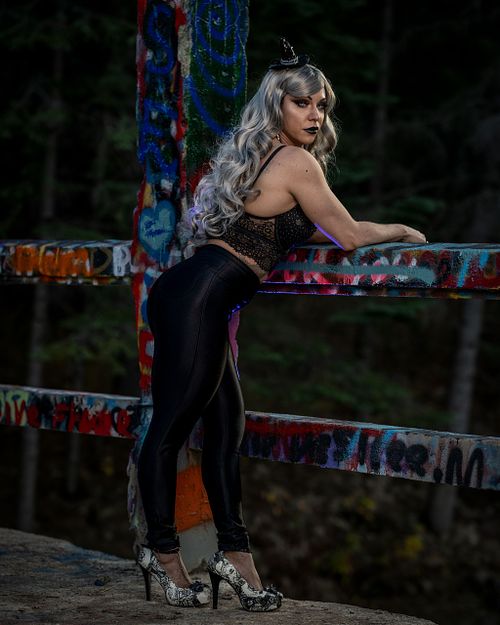 An attractive witch looks out over river from a graffitied bridge.