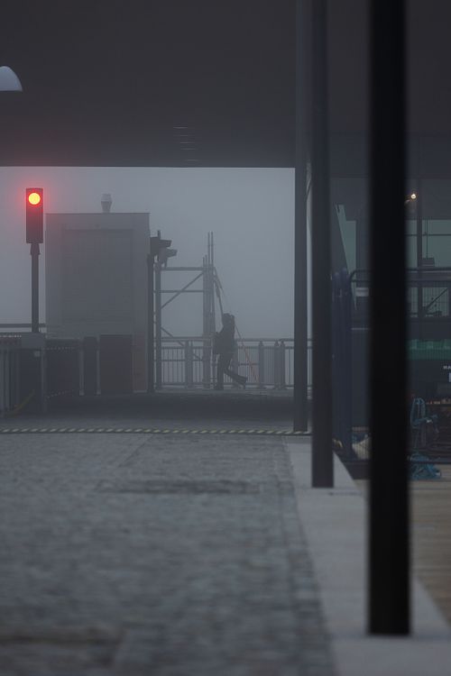 Siluett av person vid kaj i tät dimma med rött ljus i förgrunden