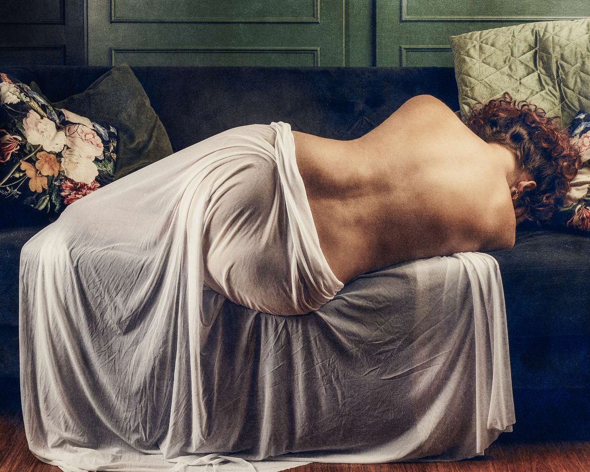 Photographie fine art d’une femme recroquevillée nue sur un canapé élégant, évoquant la maladie, la douleur invisible et la résilience humaine — œuvre de Pascal Yennis, Namur, Belgique.