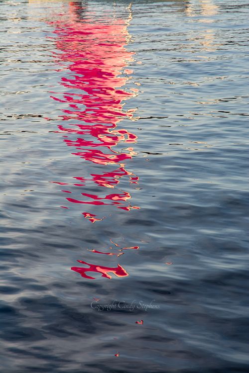 Reflection of a pink sailboat sail shimmering in the water at sunset