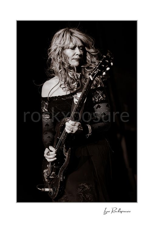 Vertical black and white image of Nancy Wilson performing with electric guitar during a Heart concert in a dramatic close stage portrait