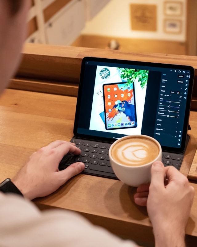 person editing a photo on a tablet with a coffee in one hand