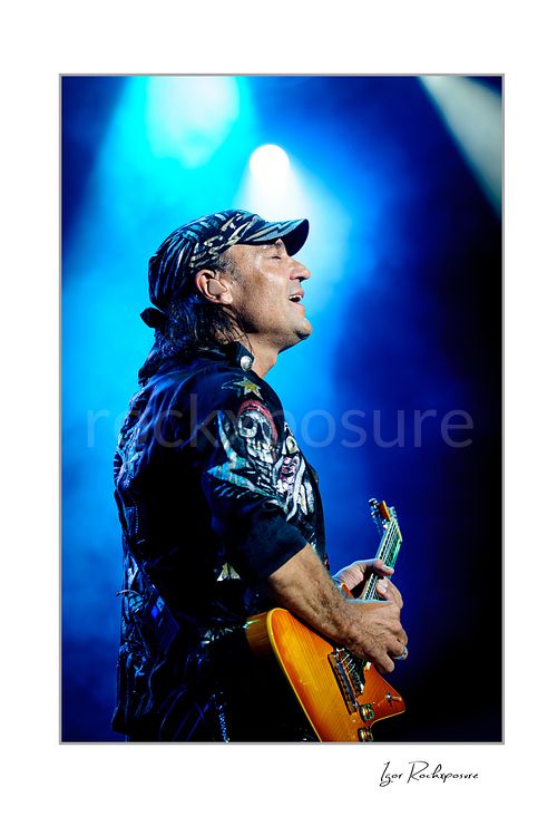 Vertical color image of Rudolf Schenker of Scorpions playing guitar live in profile under blue stage lights