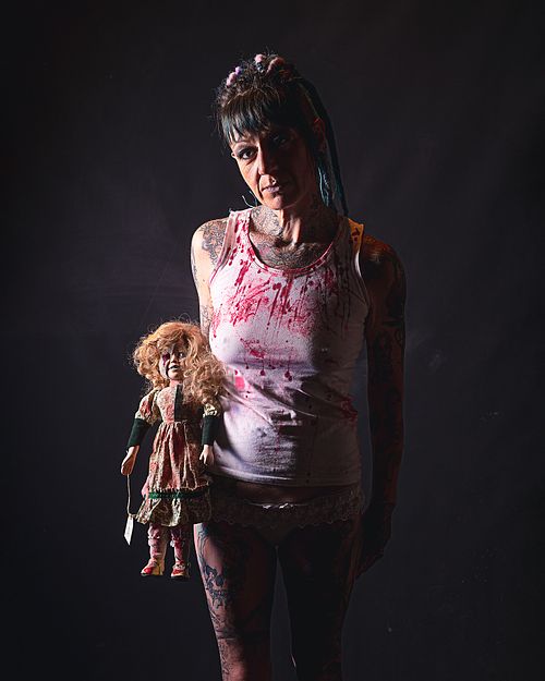 photo tarot La Psychopathe, femme sombre avec poupée délabrée, sourire mélancolique dans une ambiance lunaire