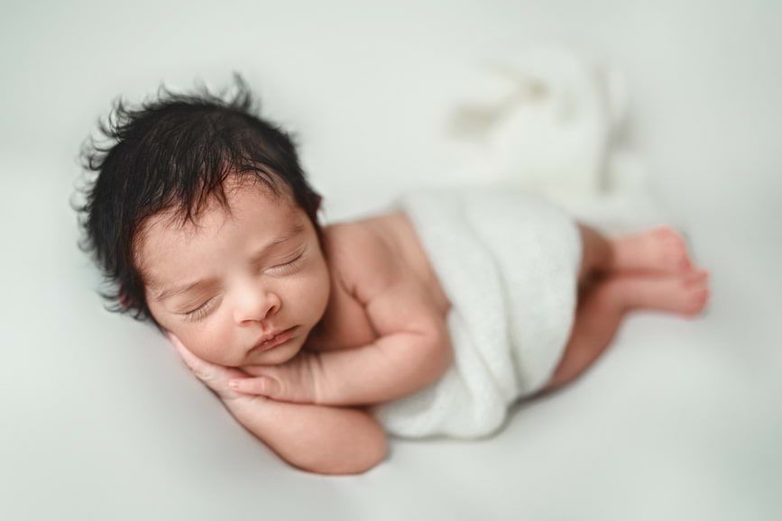 Swaddled newborn baby peacefully sleeping in a cream blanket, captured by Houston newborn photographer Amanda Mandola.