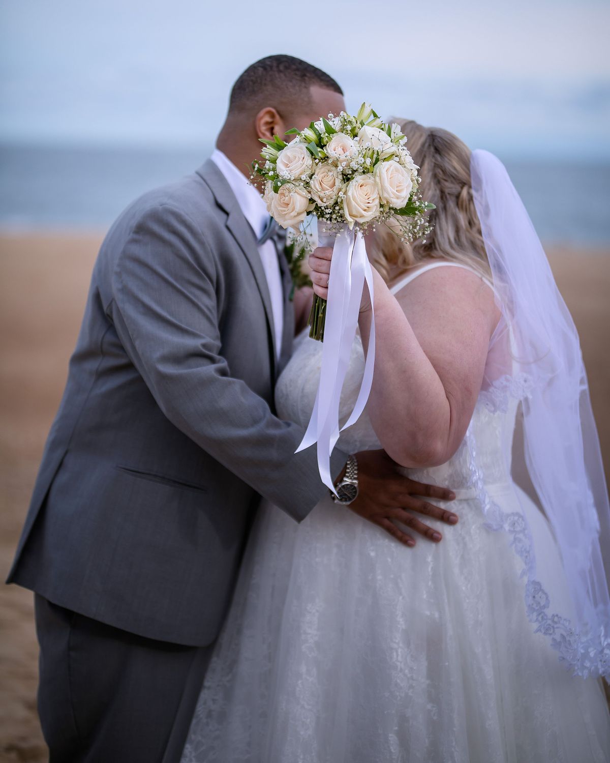 bride and groom kissing behind flower bouquet on the beach in ocean city in october during sunset