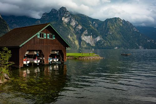Cabane en bois au bord d’un lac alpin, montagnes en arrière-plan.