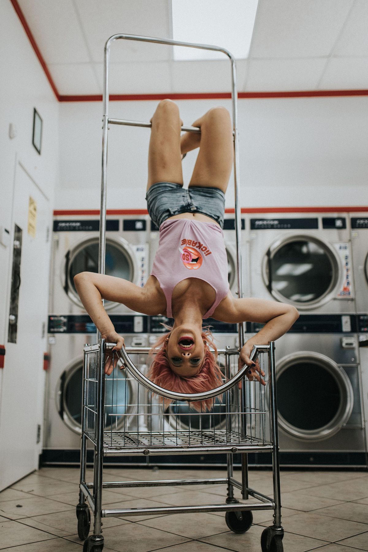 Quirky boudoir photo of woman hanging in a laundry cart inside a laundromat.