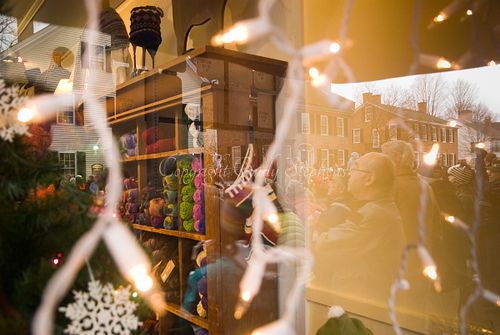 Reflection of a Christmas parade in a craft shop window, highlighting civic pride in Woodstock, Vermont.