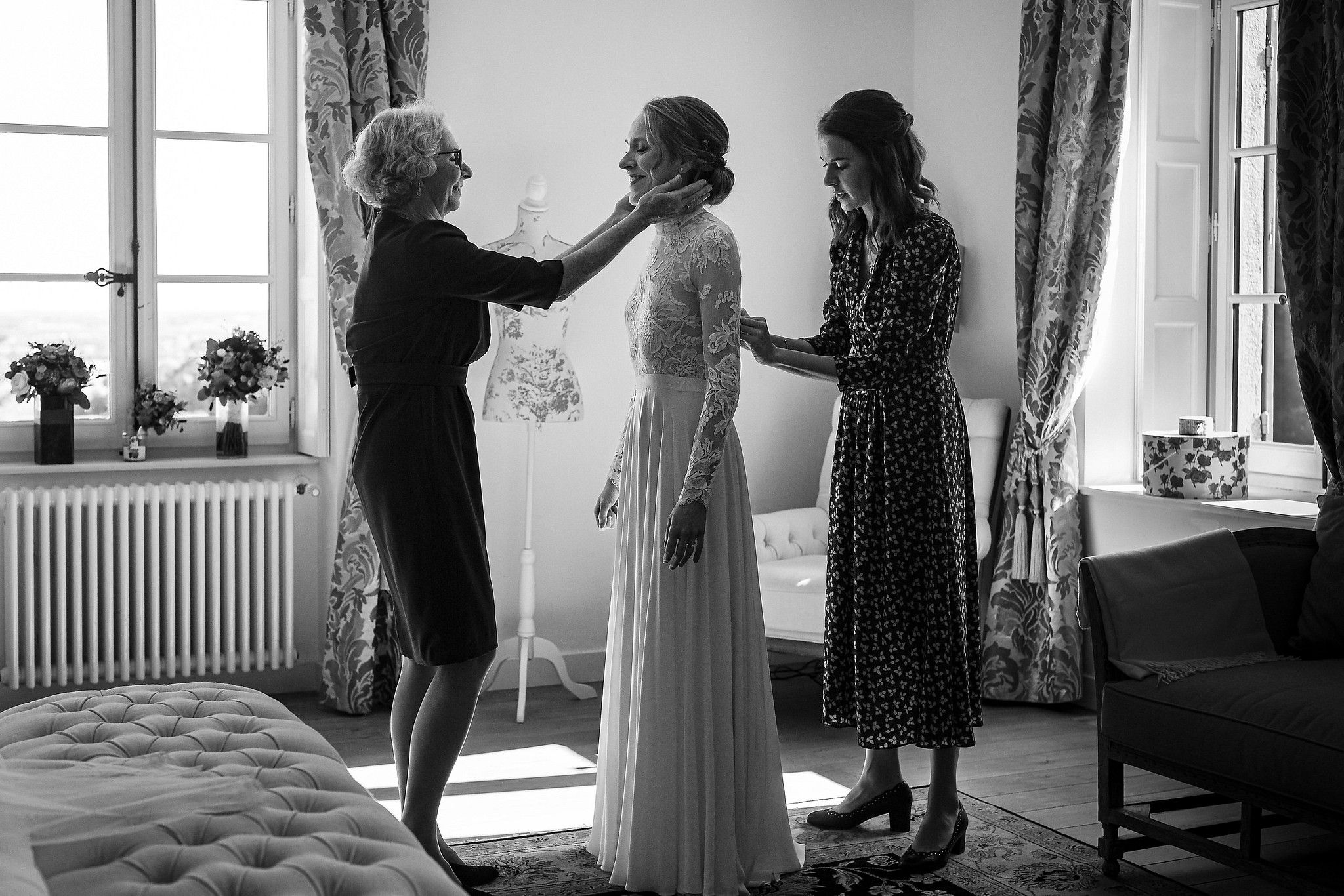 Maman de la mari&eacute;e qui lui caresse la joue pendant que sa s&oelig;ur lui met sa robe captur&eacute; par S&eacute;bastien CLAVEL photographe de Mariage &agrave; Lyon et Gen&egrave;ve