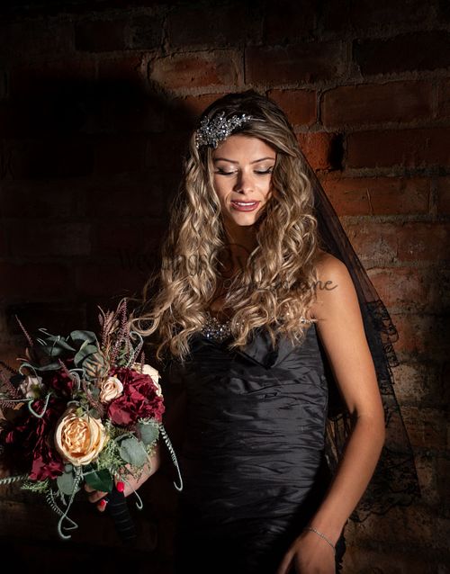 Model wearing a black wedding dress from Bridal Re-Loved Leicester, looking down while holding a bouquet, photographed by Weddings by Jermaine, with hair and makeup by Justaboutweddingshair and beauty, and accessories by Sydney Grace Bridal