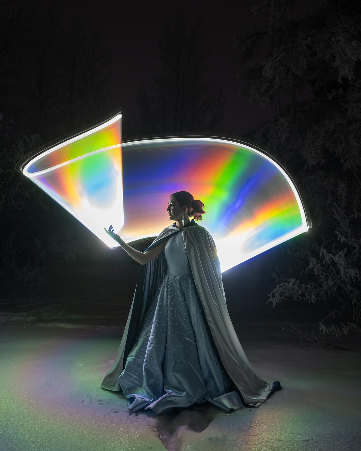 Cinderella standing in the snow wrapped with a rainbow of light.