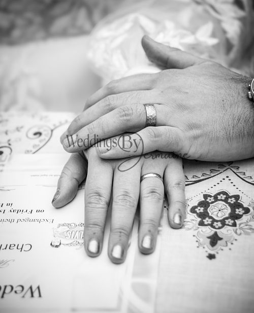 Black and white close-up of husband and wife holding hands, showcasing their wedding rings, captured by Weddings By Jermaine.