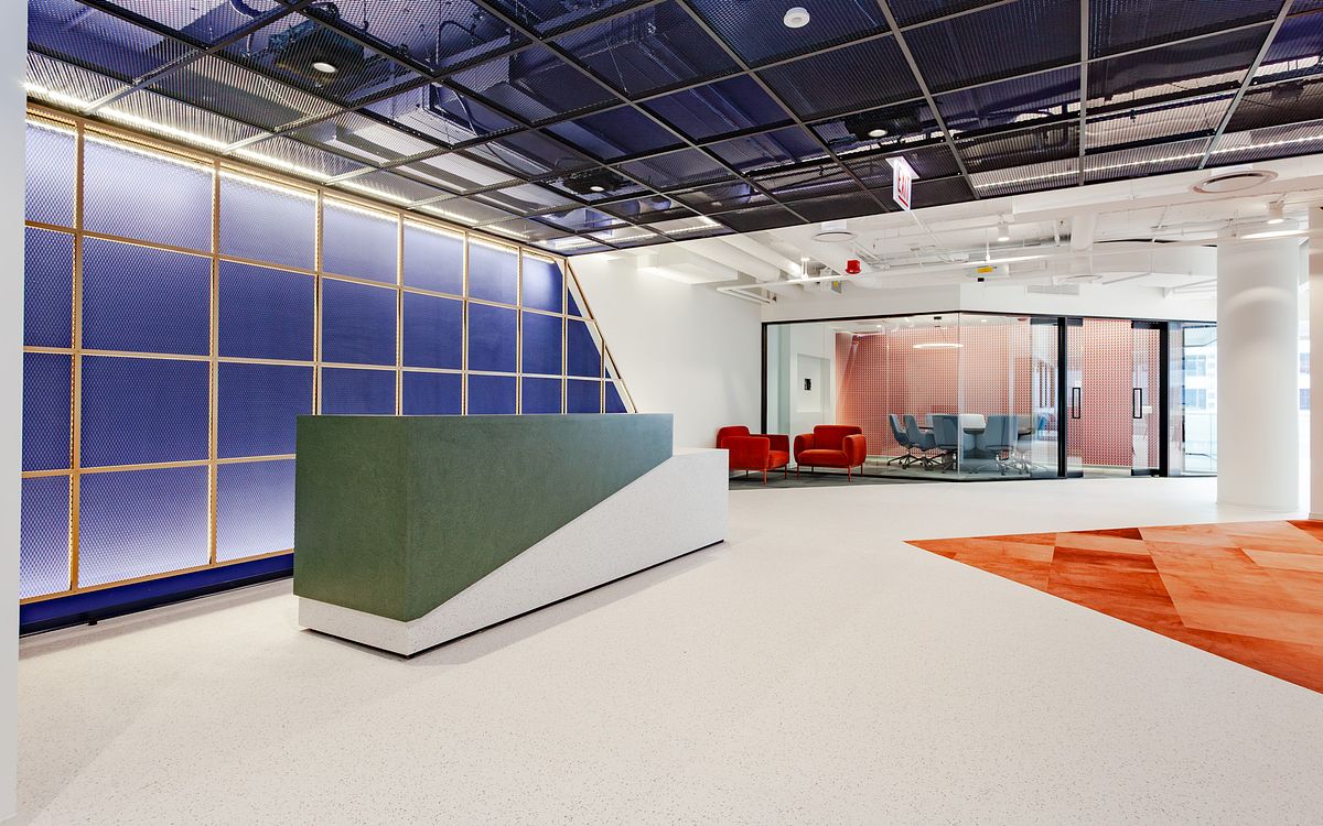 A modern office reception area at 1 South Wacker in Chicago featuring a geometric green and white desk, a blue iluminated grid wall, and a patterned orange carpet inlay.