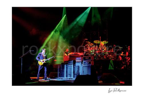 Horizontal color image of Joe Bonamassa performing live on stage with his guitar under dramatic green and red lighting
