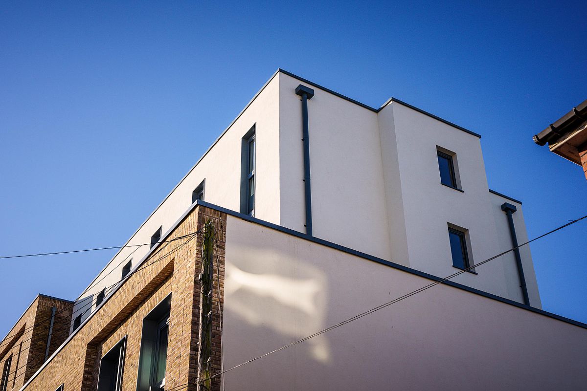 Exterior view of a section of the Easy Hotel Dublin, showcasing the contrast between the white rendered upper floors and the brick lower section. Rectangular windows are visible. A clear blue sky is in the background
