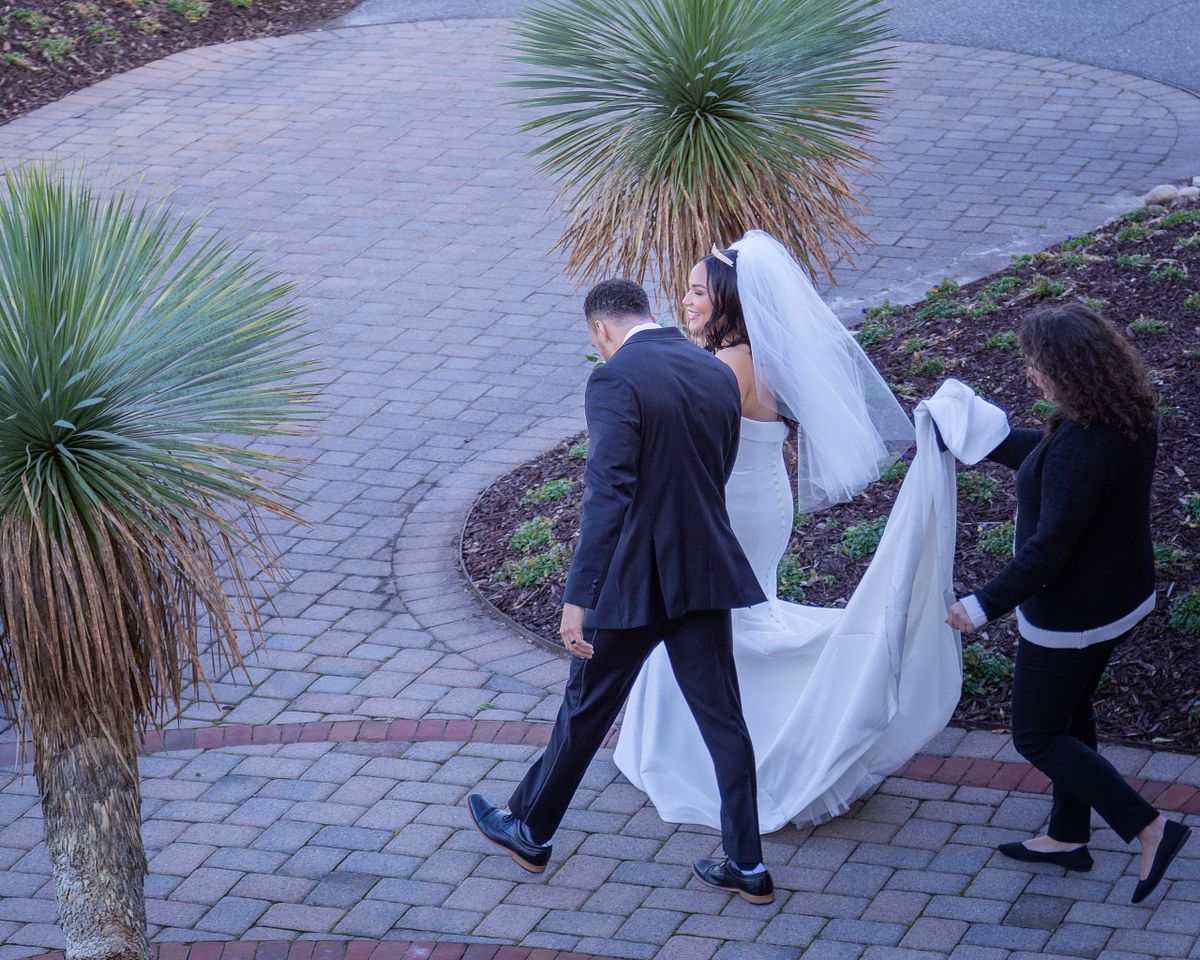 bride and groom walking between the palm trees, the bride's train is carried by her mom