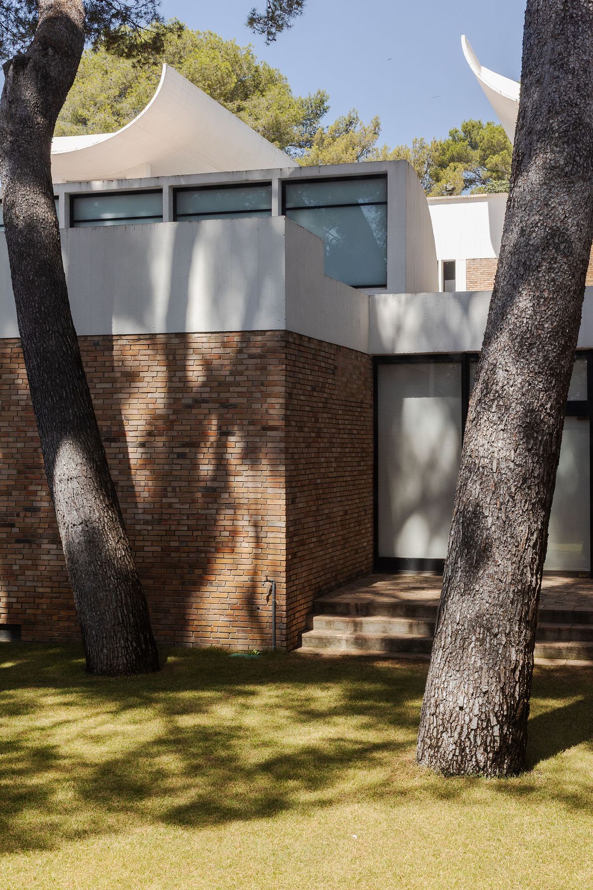 Modernistisk byggnad med tegel och vit betong mellan tallar, fotograferad i dagsljus.