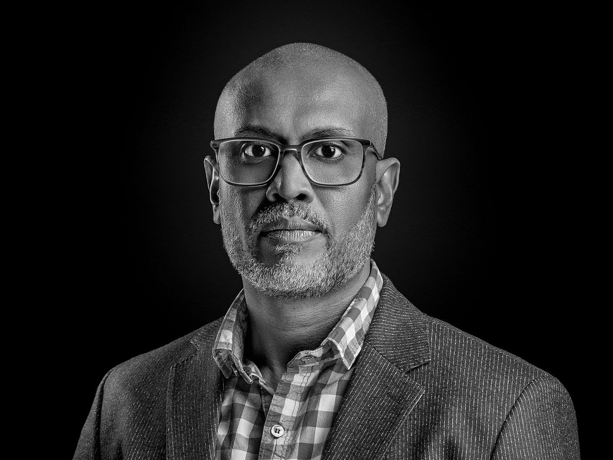 confident male executive with glasses in structured blazer, strong chiaroscuro lighting, portrait photography