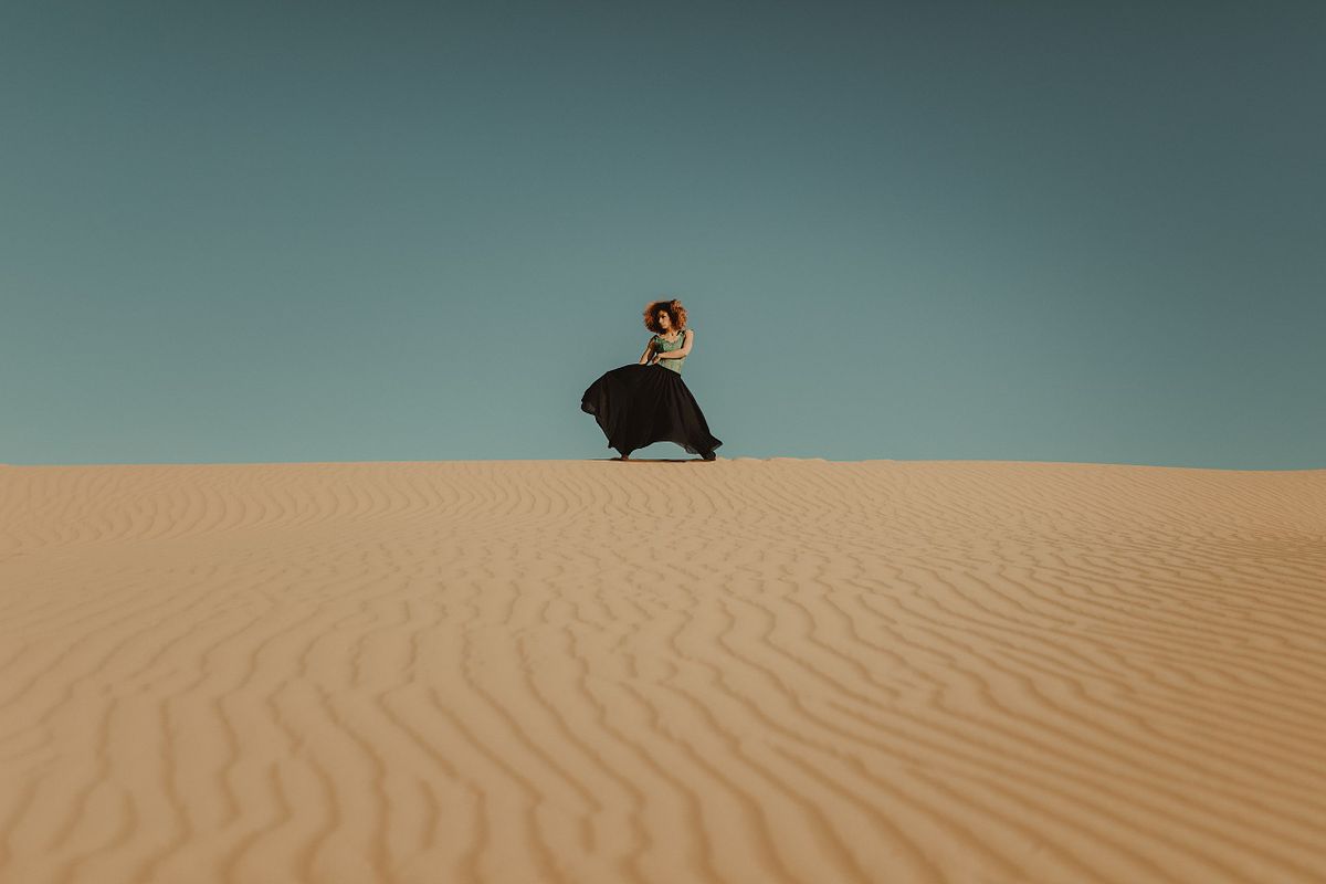 High-impact fashion portrait of a woman standing in the sweeping Yuma sand dunes of Arizona, showcasing movement, strength, and desert elegance against endless golden curves.