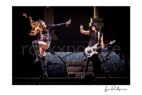 Horizontal color image of Rihanna and Nuno Bettencourt performing on stage with Rihanna mid-kick, flying hair, and a gold microphone