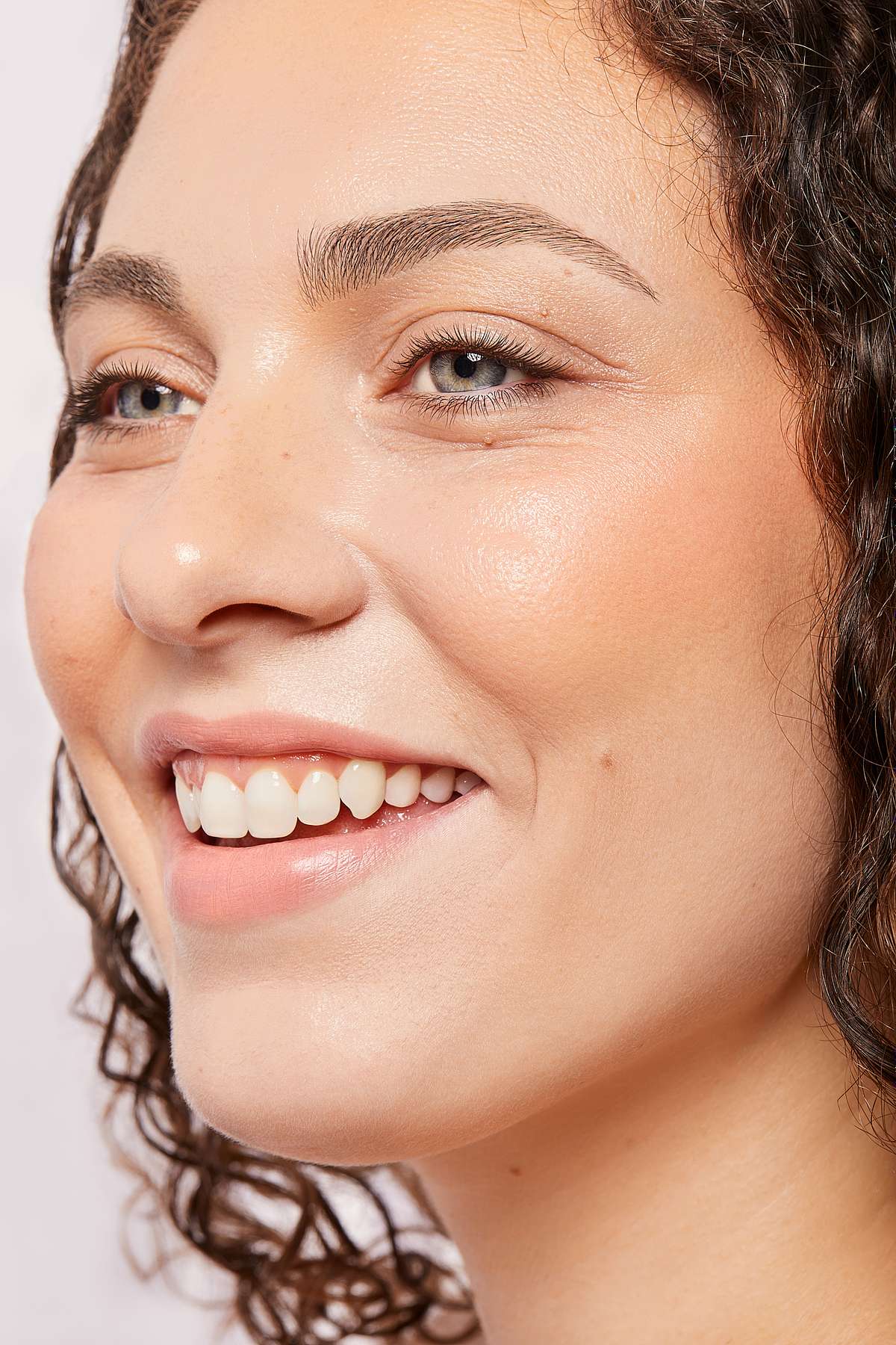 Close-up profile of a woman with curly hair, natural makeup, and a bright, genuine smile.