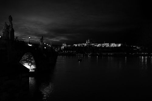 La ville s’étend dans la nuit, éclairée par le château. Une scène vaste, silencieuse, où l’eau reflète les dernières lueurs du jour.